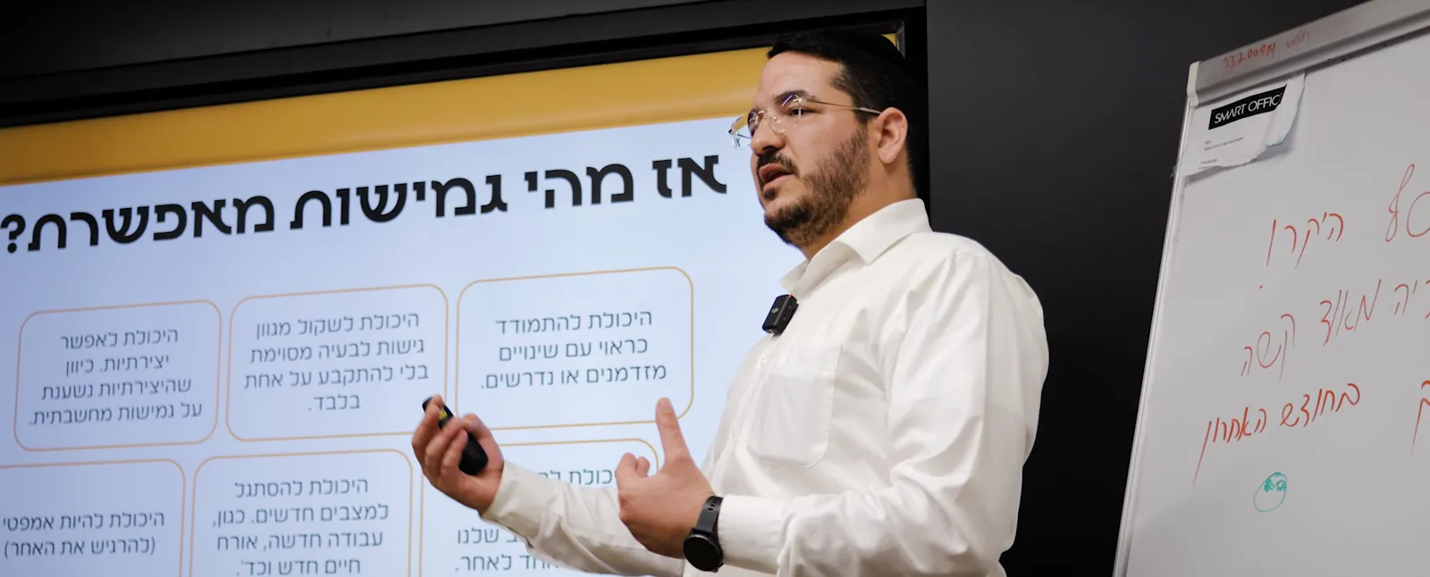 יוסף בן שושן מרצה מול כיתה, ליד מצגת ולוח